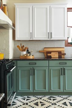 a kitchen with green cabinets and black stove top in the center, white cupboards on both sides