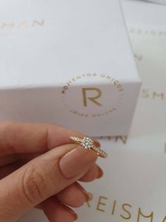 a woman's hand holding an engagement ring in front of a box with the letter r on it