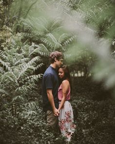 a man and woman standing in front of some trees with their arms around each other