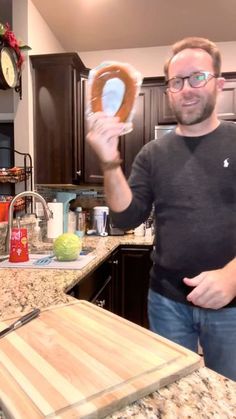 a man is holding up a pretzel in his hand while standing at the kitchen counter