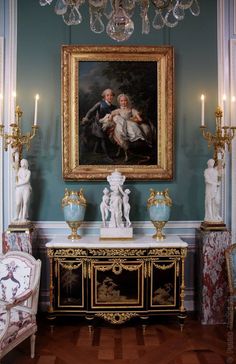 a painting hangs on the wall above a table with two statues and candles in front of it