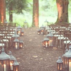 rows of chairs with lit candles on them in the middle of a wooded area surrounded by trees