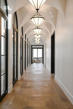 an empty hallway with wooden flooring and arched ceiling lights on either side of the doors