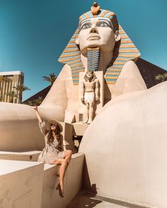 a woman sitting on the ledge of a building with an egyptian statue in the background