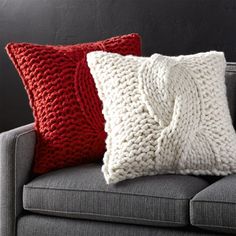 two red and white knitted pillows sitting on a gray couch next to each other