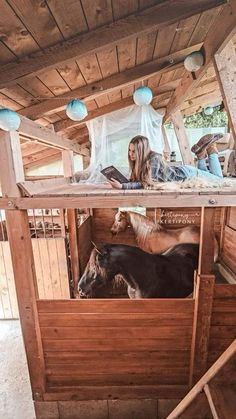 a woman sitting on top of a wooden structure next to two goats in a pen