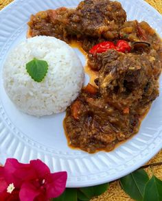 a white plate topped with meat and rice next to a pink flower on a table