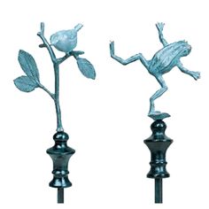 two metal frog sculptures sitting on top of each other, one holding a flower and the other