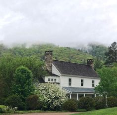 a white house sitting on the side of a lush green hillside next to a forest