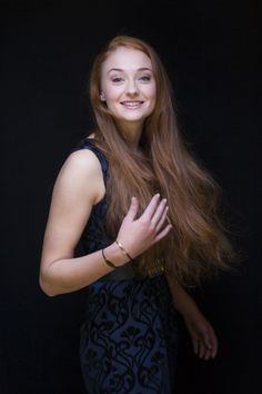 a woman with long red hair standing in front of a black background posing for the camera