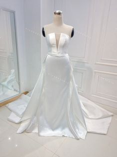 a white wedding dress on display in front of a mirror and mannequins