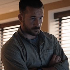 a man with his arms crossed standing in front of blinds