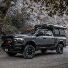 a black truck parked on the side of a road next to some trees and rocks