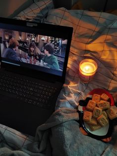 an open laptop computer sitting on top of a bed next to a plate of food