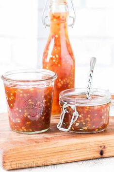 two jars filled with jam sitting on top of a wooden cutting board