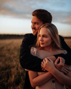 a man and woman embracing each other in the middle of a field at sunset or sunrise