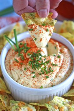 a hand holding a tortilla chip over a bowl of dip