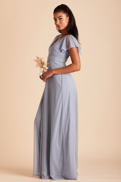 a woman in a blue dress is holding a dried flower and looking at the camera