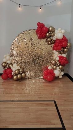 a large gold and red balloon arch in the middle of a room with wooden floors