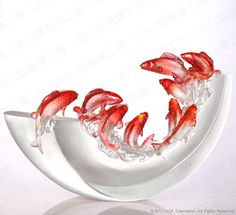 five red fish in a white bowl with water on the bottom and one above it