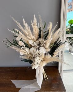 a bouquet of dried flowers on a table in front of a window with white ribbon