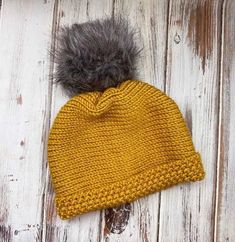 a yellow knitted hat with a grey pom - pom sitting on top of it