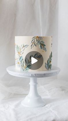 a white cake with leaves on it sitting on a plate next to a white backdrop