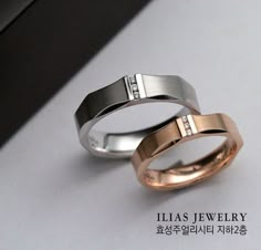 two wedding rings with diamonds on them sitting next to each other in front of a window