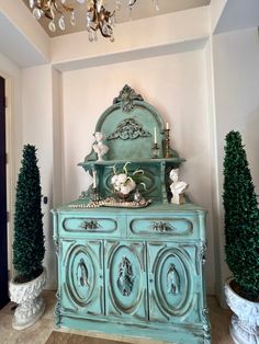 a blue dresser with some potted plants on top and a chandelier hanging from the ceiling