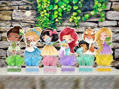 paper cut outs of disney princesses on display in front of a stone wall with ivy