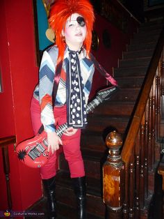 a woman with red hair and makeup is holding a guitar in her hand while standing on the stairs