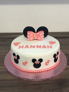 a white cake with pink and black minnie mouse ears on it's top is sitting on a wooden table