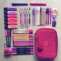 various pens and pencils are laid out on a table next to a pink bag