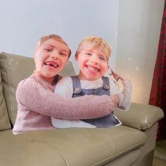 two young boys sitting on top of a couch with their arms around each other's shoulders