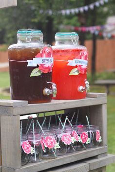 some drinks are sitting on top of a wooden shelf in the grass and one is filled with liquid