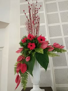 a white vase filled with red flowers and greenery