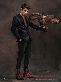 a man holding an owl in his right hand while standing next to a dark background