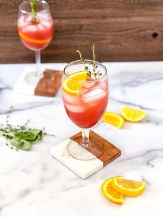 two glasses filled with pink lemonade and garnished with fresh herbs on a marble table