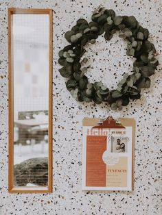 a bulletin board with a wreath on it next to a mirror and clipboard attached to the wall