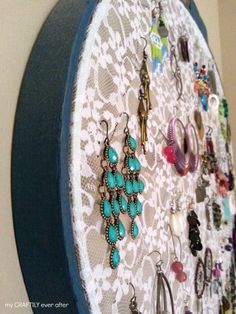 there are many earrings hanging on the wall in front of the mirror with lace around it