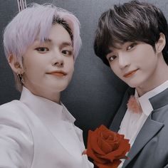 two young men posing for a photo with one holding a rose in front of the other