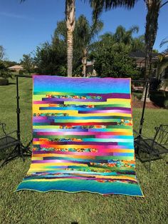 a colorful quilt on the grass in front of a palm tree and lawn chaires