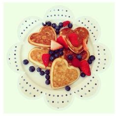 heart shaped pancakes with berries and blueberries on a white polka dot plate in the shape of a flower