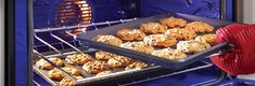 a person holding a tray of cookies in front of an oven with it's door open