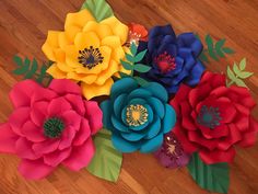 paper flowers are arranged on a wooden floor with green leaves and red, yellow, blue, and orange flowers