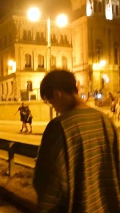 a man standing in front of a building at night with his back to the camera