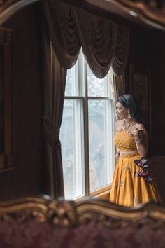 a woman standing in front of a window looking at herself in the mirror with her hand on her hip