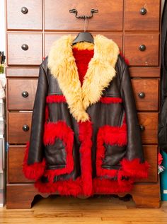 a leather jacket with red and yellow fur on it, hanging from a wooden dresser