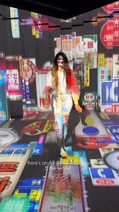 a woman walking down a street in front of advertisements on the wall and floor,