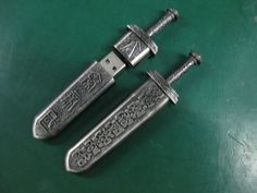 two silver colored swords are on a green surface with an intricate design and ornate designs